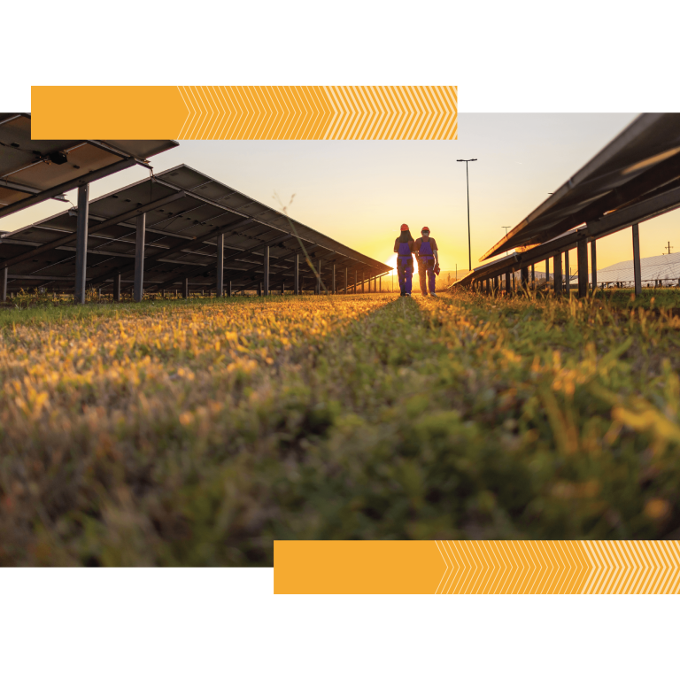 Two solar technicians walk through a solar farm toward a rising sun